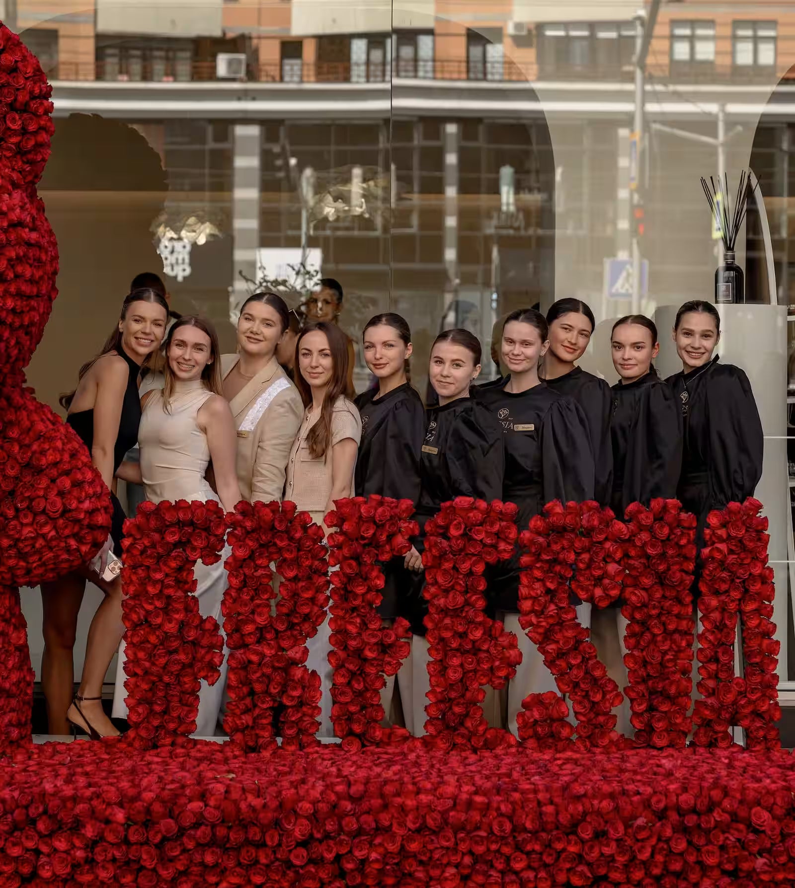 Group of women posing in front of large red rose floral arrangement spelling out FREESIA, flower shop setting.