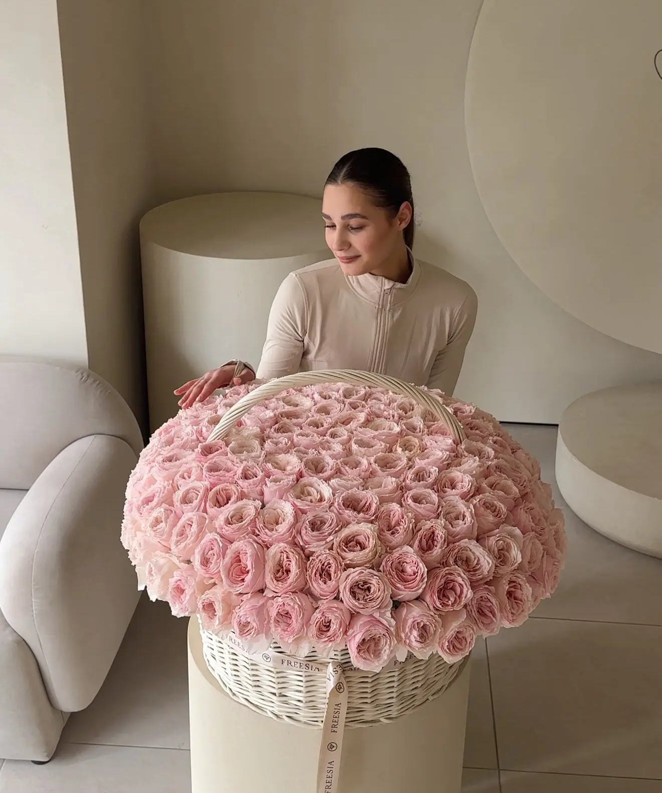 Woman with large basket of pink roses in a modern, neutral-toned interior