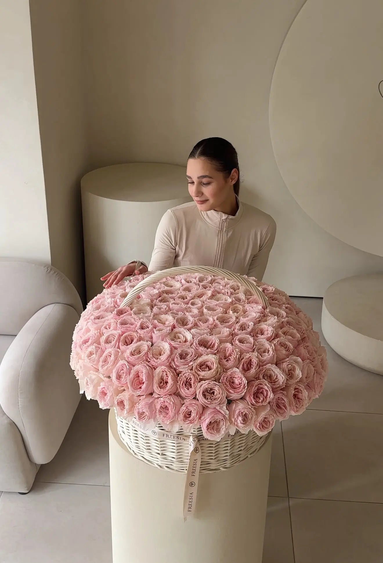 Woman with large basket of pink roses in a modern, neutral-toned interior