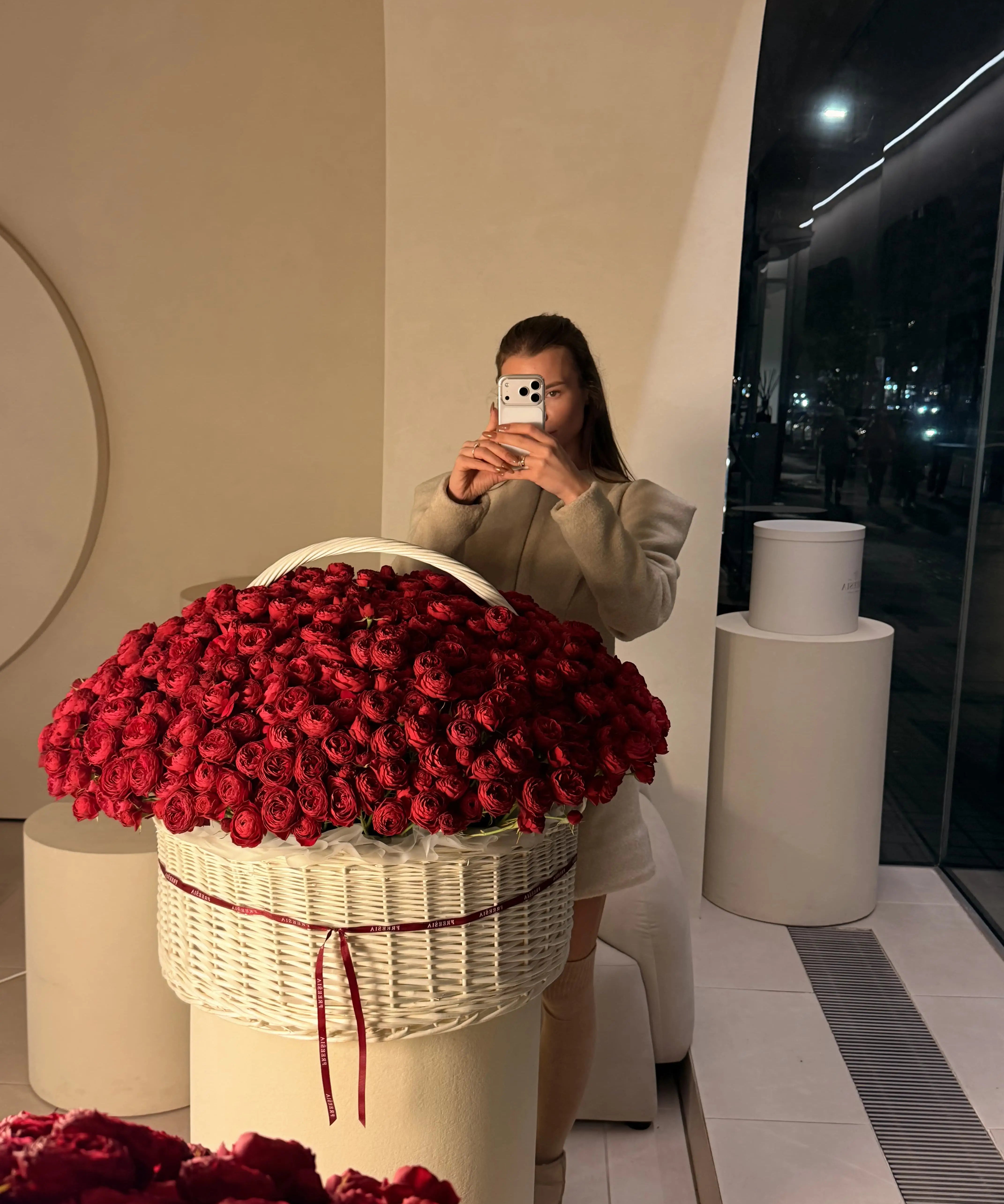 Large white basket of fresh red roses with a ribbon, woman taking photo in modern floral studio