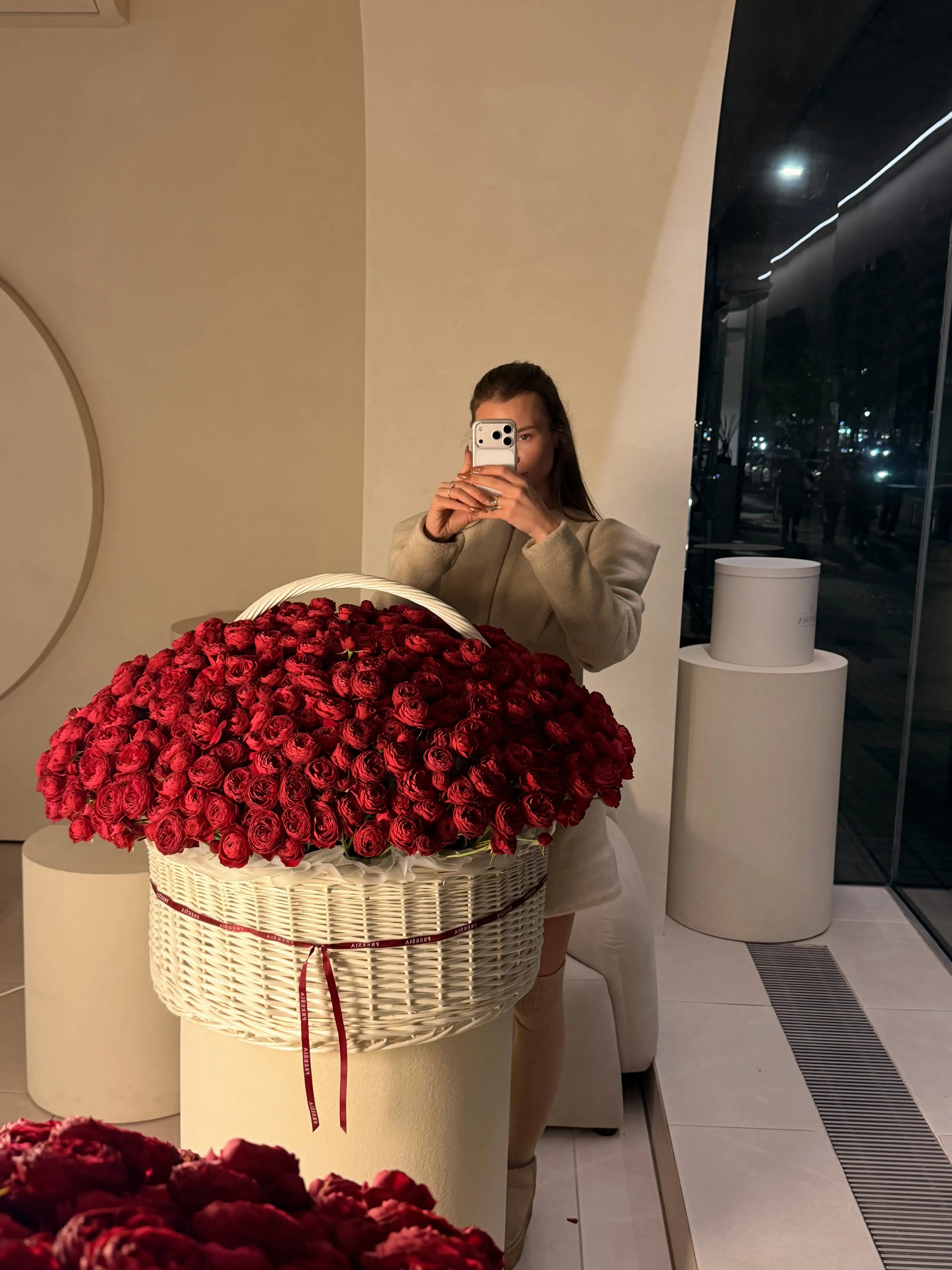 Large white basket of fresh red roses with a ribbon, woman taking photo in modern floral studio